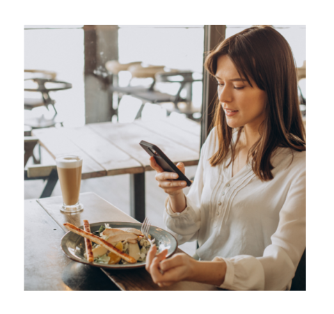 Persona sentada en un café, sosteniendo un teléfono móvil mientras disfruta de un plato de comida y una bebida.